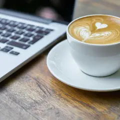 Kawa latte z sercem na piance obok laptopa. Idealny moment na picie kawy po operacji zaćmy i powrót do codzienności.