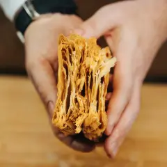 Manos sostienen un trozo de masa de hojaldre casera, mostrando sus finas y crujientes capas doradas.