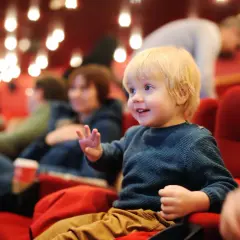 Mały chłopiec z blond włosami siedzi w kinie, ciesząc się filmem. Czy w kinie sprawdzają wiek dziecka?