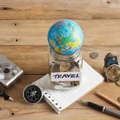 Bocal rempli de pièces avec un globe, un appareil photo, une boussole et un carnet, prêt pour le backpacking en Europe.