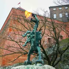 Smok Wawelski ziejący ogniem, pomnik nawiązujący do legendy, na tle ceglanych murów Wawelu.