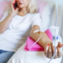Frau erhält Infusion, während sie telefoniert. Thema: Brustkrebs HER2 und Lebenserwartung.