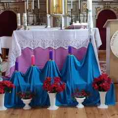 Ołtarz kościelny udekorowany na adwent: świece, kwiaty i figurka.