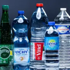 Une rangée de bouteilles d'eau minérale, dont Perrier, Vittel et Contrex, évoque le scandale de l'eau en bouteille.