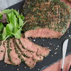 Saftiges Flank Steak, mariniert und perfekt gegrillt, mit frischem Salat und Gewürzen auf einem Schieferbrett serviert.
