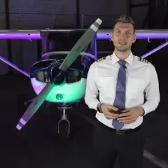 Mężczyzna w stroju pilota przed samolotem, oświetlonym kolorowymi światłami. Chcesz wiedzieć, jak zostać pilotem?