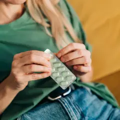Kobieta w zielonej bluzce trzyma opakowanie zielonych tabletek. Może to być lek na przeziębienie, suplement diety, albo coś na poprawę nastroju, jak np. vabinxo.