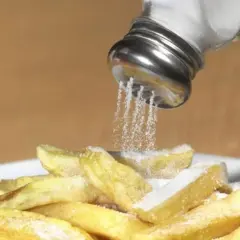Salzstreuer rieselt Salz auf Pommes. Zu viel Salz essen kann zu Problemen führen.