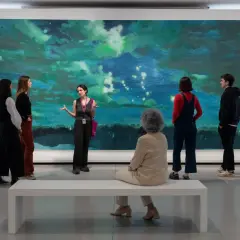 Visite guidée d'une œuvre d'art abstraite aux teintes bleues et vertes, évoquant une scène céleste. Un groupe écoute attentivement, comme à la bourse du commerce.
