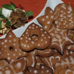 Stos pierniczków z ziemniakami w kształcie gwiazdek i serduszek, ozdobionych lukrem. Obok świąteczna dekoracja z szyszką.