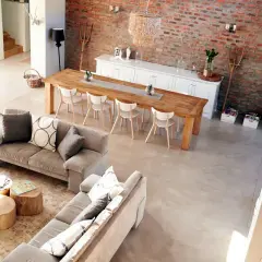 Nowoczesny salon w stylu rustykalnym z ceglaną ścianą, drewnianym stołem i wygodnymi sofami.