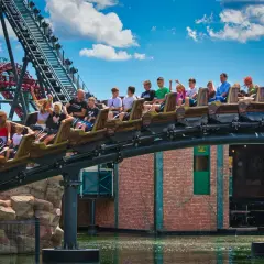 Energylandia otwarcie: wagoniki kolejki górskiej z pasażerami pędzą nad wodą, radość i emocje w parku rozrywki.