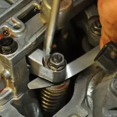 Mechanik reguluje zawory w silniku, używając śrubokręta i szczelinomierza.