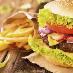 A close-up of a gourmet hamburger with lettuce, tomato, onion, bacon, and cheese, next to a bag of french fries.