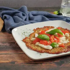 Eine köstliche low carb pizza mit Tomaten, Mozzarella und Basilikum auf einem weißen Teller.