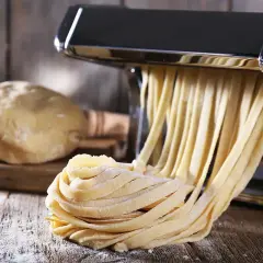 Świeży makaron domowy, przygotowany według przepisu babci, wychodzi z maszynki. Obok leży kulka ciasta.