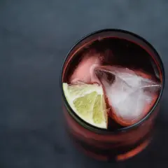 Szklanka z ciemnym napojem, lodem i plasterkiem limonki. Idealny drink z Asbach Uralt, by poczuć smak lata.