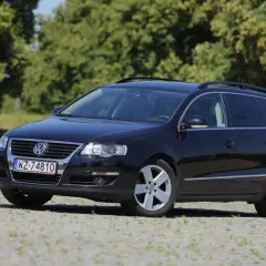 Czarny Volkswagen Passat kombi, model r36, zaparkowany na kamienistym podjeździe, z zielonymi drzewami w tle.