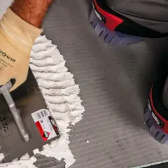 Pose d'enduit avec une truelle crantée pour le carrelage. Le choix du bon taille peigne carrelage est essentiel pour une pose parfaite.