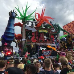 Folla festante alla Love Parade Zurigo, con carri colorati, un drago blu e un'ape gigante.