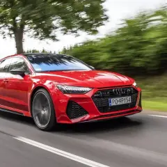 Czerwone Audi RS7 pędzi po drodze, otoczone zielenią drzew.