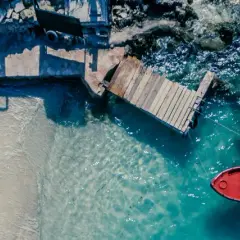 Traumhafter Urlaub im August: Sandstrand, Holzsteg und ein rotes Boot im türkisfarbenen Meer.