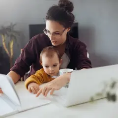 Mama z dzieckiem przy biurku, pracująca zdalnie. Kosiniakowe dla kogo? Dla wszystkich rodziców łączących pracę z opieką nad dzieckiem.