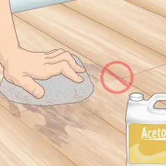 Main tenant, ne pas enlever peinture sur lino avec acétone. Une main frotte le sol avec une éponge.