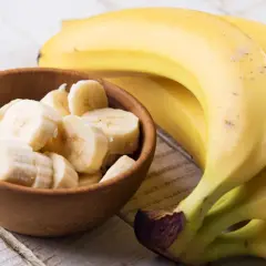 Dojrzały banan kcal w miseczce i pęczek bananów na drewnianym stole.