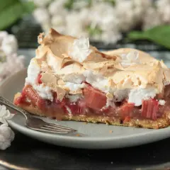 Kawałek ciasta kruchego z rabarbarem i bezą, ozdobiony kwiatkami. Idealny na wiosenne popołudnie.