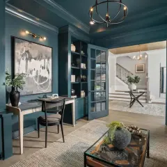 A study with a striking color drenching in deep teal. Built-in bookshelves, a desk, and French doors create a sophisticated workspace.