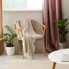 A cozy reading nook with a wicker chair draped in a blanket, flanked by pooled curtains in soft peach and dusty rose hues.