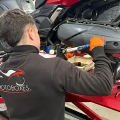 Mecánico con guantes naranjas realiza cambio de aceite a moto. Consulta el precio del cambio de aceite de moto y el aceite Motul.