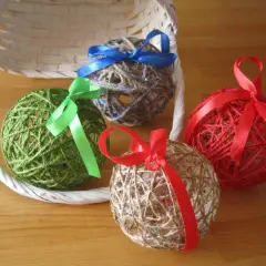 Palline decorative fatte con spago e colla vinilica, decorate con nastri colorati, appoggiate vicino a un cestino bianco.