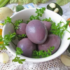 Fioletowe jajka w zalewie, ozdobione natką pietruszki, obok kolorowych pisanek i czosnku.