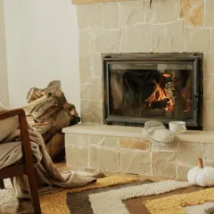 Przytulny kominek na poddasze z palącym się ogniem, obok stos drewna i wygodny fotel.