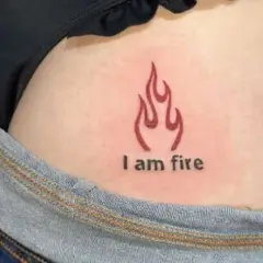 Płomień i napis "I am fire" na skórze, subtelny tatuaż na pośladku.