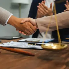 Uścisk dłoni prawników przy biurku z młotkiem sędziowskim i wagą sprawiedliwości. Zastanawiasz się, ile zarabia sędzia?