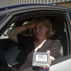 Kvinna i bil svettas och håller upp en termometer som visar 49,3 grader. Det är så varmt att bilen blir inte varm.