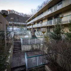 Opuszczone miasta w Polsce: zaniedbany hotel z widokiem na wzgórza, zarośnięte schody i zniszczone balustrady.