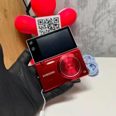 Czerwony aparat Samsung MV800 z obracanym ekranem, trzymany w czarnej rękawiczce.