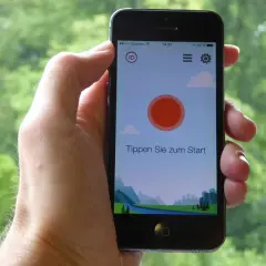 Ein Smartphone wird gehalten, um Vogelstimmen vorspielen zu lassen. Die App zeigt eine Landschaft und den Text "Tippen Sie zum Start".