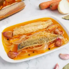 Dos filetes de caballa en escabeche, con zanahoria, cebolla y ajos, en una bandeja blanca.