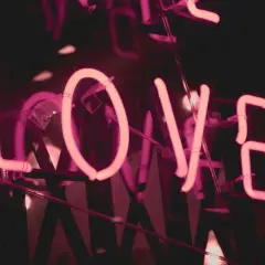 Lettere al neon rosa formano la parola "LOVE", un invito a dedicare una canzone per una persona speciale in italiano.