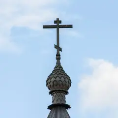 Drewniany krzyż na kopule cerkwi, symbol gruzińskiej religii prawosławnej, na tle błękitnego nieba z chmurami.