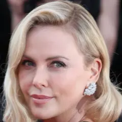 Charlize Theron mit eleganten Frisuren mit Wirbel am Hinterkopf, glitzernden Ohrringen und einem strahlenden Lächeln.