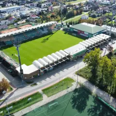 Widok z lotu ptaka na stadion Górnik Łęczna z zieloną murawą, trybunami i otaczającymi go budynkami.