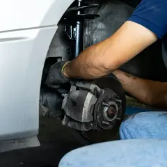 Mecánico trabajando en el sistema de frenos y amortiguadores de un coche. Merece la pena cambiar amortiguadores para una conducción segura.
