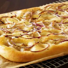 Focaccia dorada con finas rodajas de cebolla balsámica y sal gruesa, recién salida del horno.