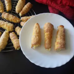 Chrupiące rurki z kremem budyniowym, posypane cukrem, kuszą swoim wyglądem. Kilka na talerzu, reszta na kratce.